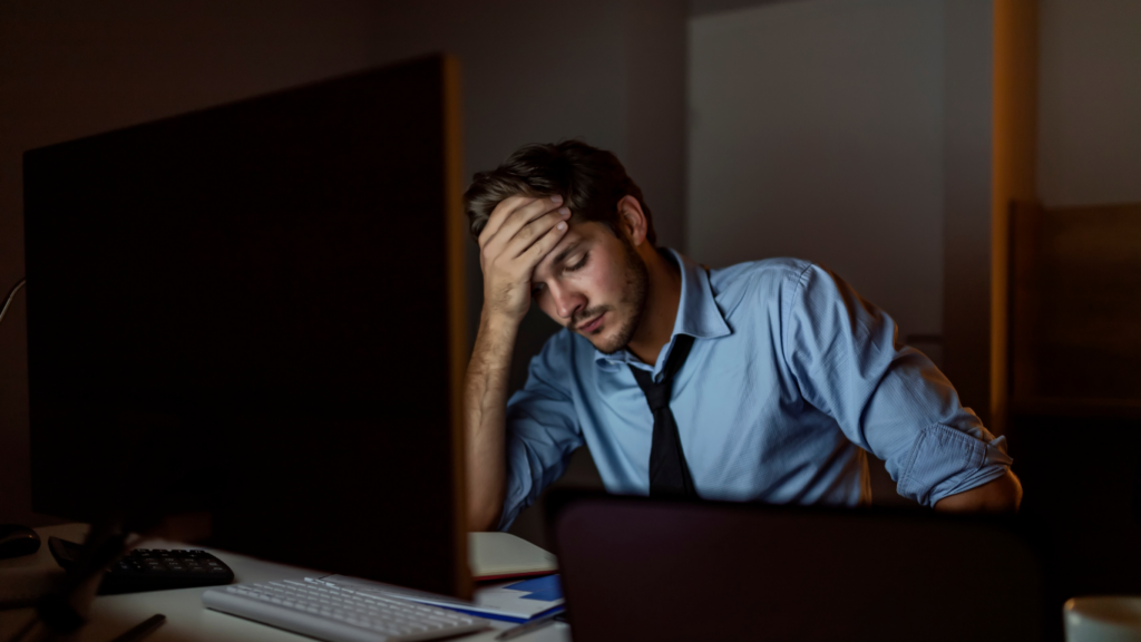 business man with his hand on head stressed in the dark at his computer desk